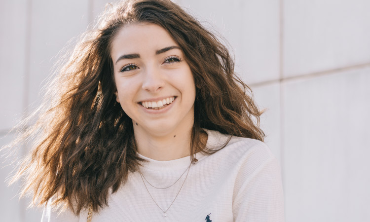 Brunette young woman with crimped hair smiles while wearing a Ralph Lauren polo sweater and a two strand necklace