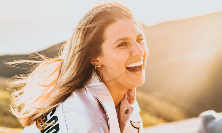 Closeup of a blonde woman smiling while wearing Invisalign clear removable trays as the sun sets