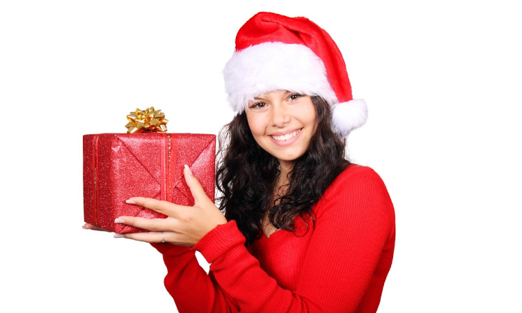 smiling girl in red sweater and santa hat holding a red present