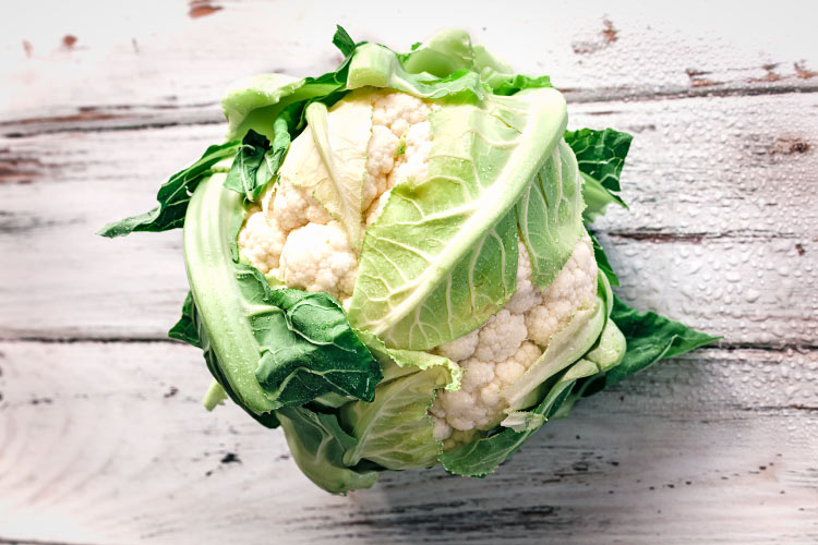 Aerial view of a head of white cauliflower with its green leaves encasing it on a distressed wooden counter
