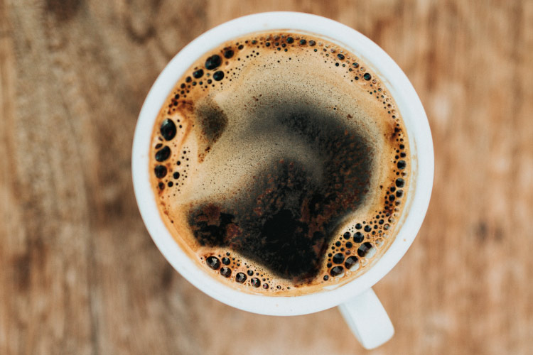 Aerial view of a white mug holding dark brown frothy coffee that can cause extrinsic stains and yellow teeth