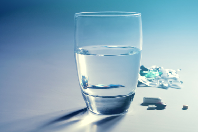 A glass of water next to a little cluster of medications that can cause yellow teeth