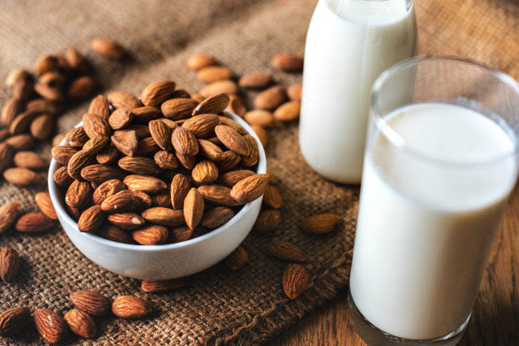 A pile of almonds in a white bowl next to 2 glass containers of white milk, foods that are good for teeth