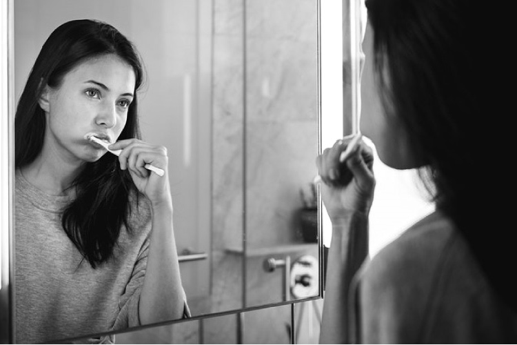 girl looking in the mirror brushing her teeth to avoid cavities