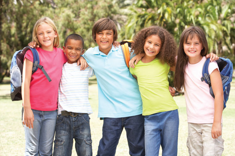 Group of elementary-age children smile together as they hold backpacks, ready for back-to-school school