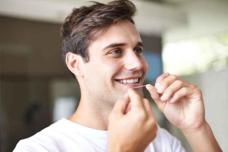 Brunette man smiles as he uses string floss to clean between his teeth every day