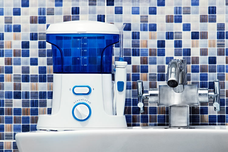 A blue and white water flosser sits on a bathroom sink in front of a blue mosaic tile wall