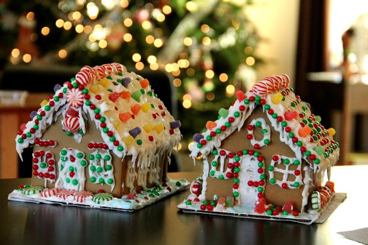 Two gingerbread houses covered in sugary candies in front of a lit Christmas tree