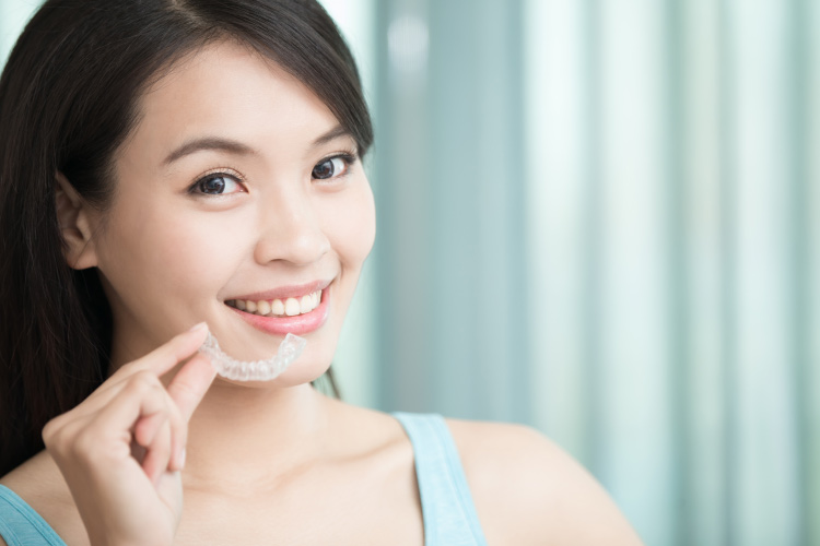 Smiling dark haired girl holding a clear aligner near her chin