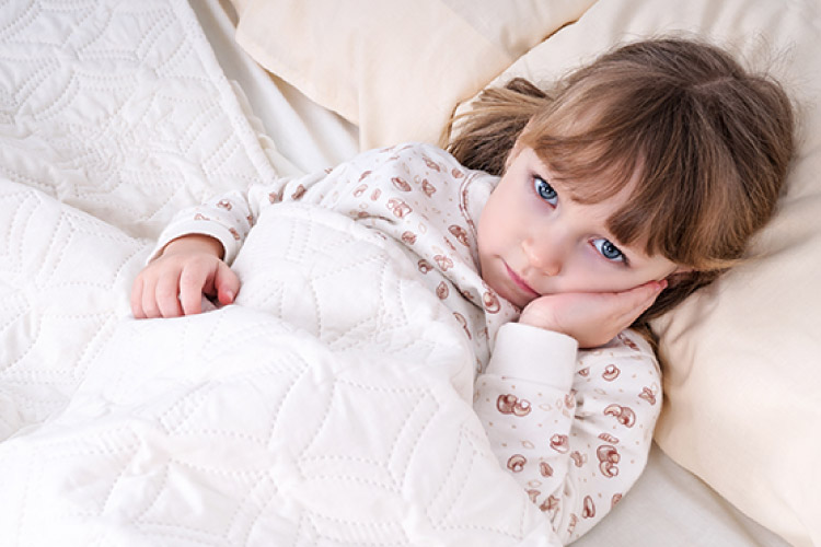 Sad little girl lying in bed with her hand over her cheek because of a toothache
