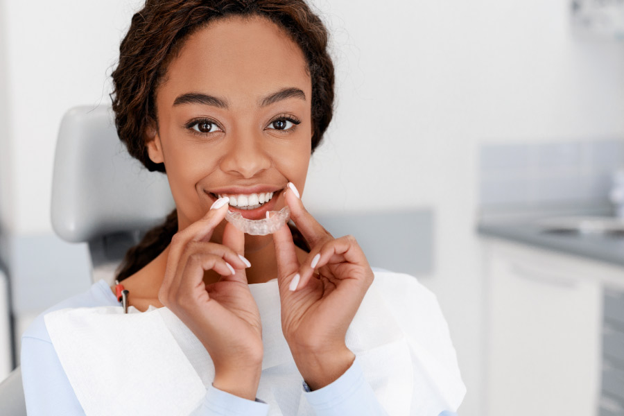 Pretty black girl smiling and holding a clear aligner