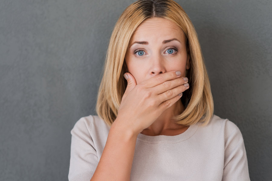 Blonde woman covering her mouth due to fear of bad breath