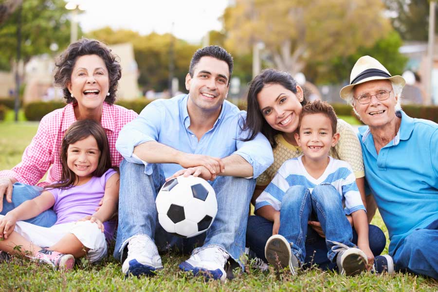 Smiling multi-generational family sitting on the grass with a soccer ball.