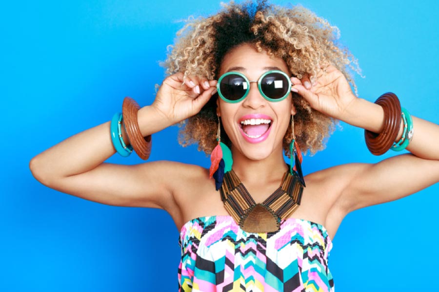 Young woman with colorful clothes, jewelry and big sunglasses and a big smile.