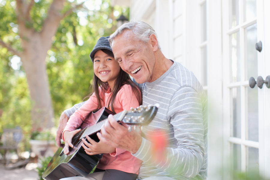 Grandfather teaching young granddaughter to play the guitar on an outdoor terrace.